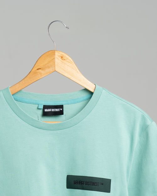 Close-up of the front SELECT DISTINCT logo on the green ORIGIN Essentials No.1 T-shirt in 100% organic cotton.